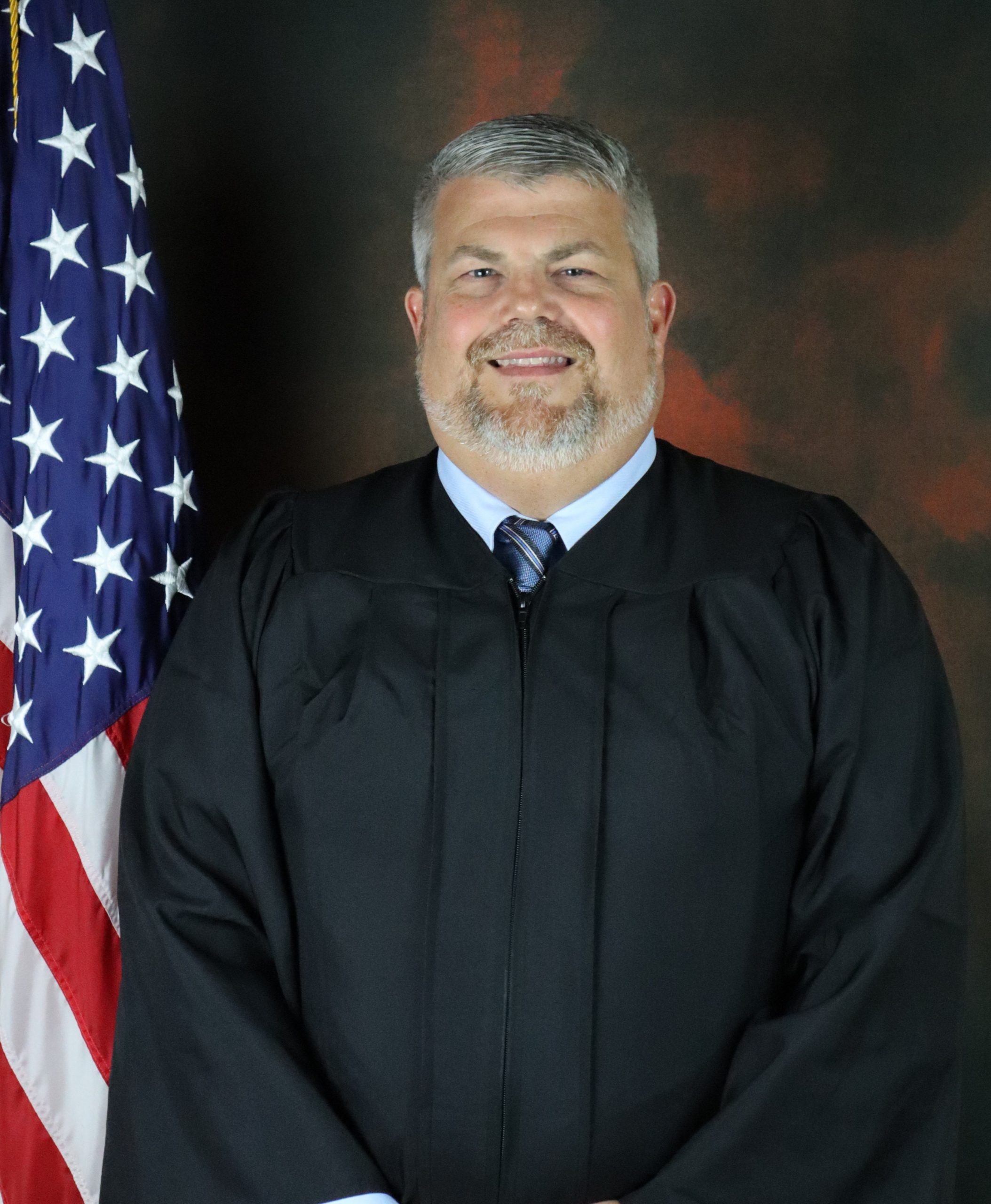 Portrait Picture of Judge Jason Smith. He is wearing his robe and is standing next to the United States flag.